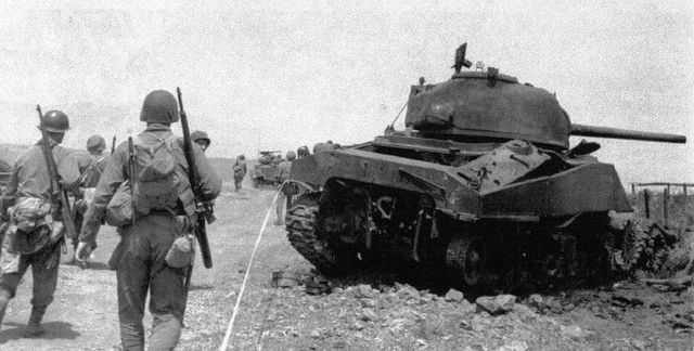 Infantería del 6th Armored Infantry Regiment pasa junto a un Sherman puesto fuera de combate en Cisterna. 22 de mayo de 1944